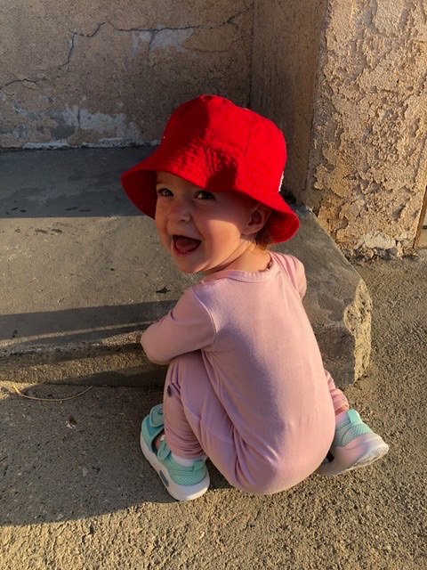 Toddler in a red hat giggles at camera