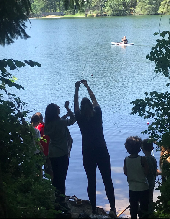 kids fishing on the shore of a lake, the oldest helping add bait to a line